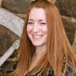 The image shows a woman with long red hair smiling at the camera.
