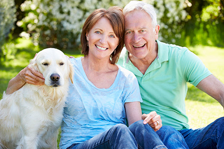 The image shows a man and woman sitting on grass outdoors with a golden retriever dog between them  they are smiling and appear to be enjoying a pleasant moment together.