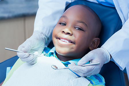 A young boy sitting in a dental chair with a smile, receiving dental care from a professional.