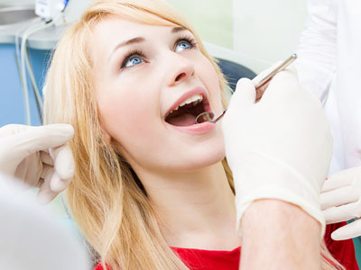 Woman undergoing dental procedure, with mouth open wide, while seated in chair with medical professionals attending to her.