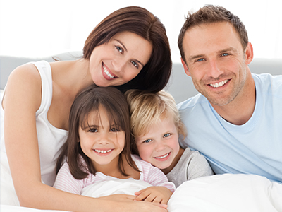 A family of five posing for a photo on a bed with smiles on their faces.